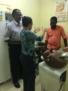 A clinician (center) practices a simulated ano-genital examination under the guidance of a clinical mentor (left).